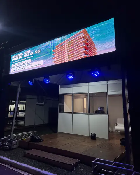 Estrutura montada à noite, com painel de LED no alto, refletores azuis e sala de vidro