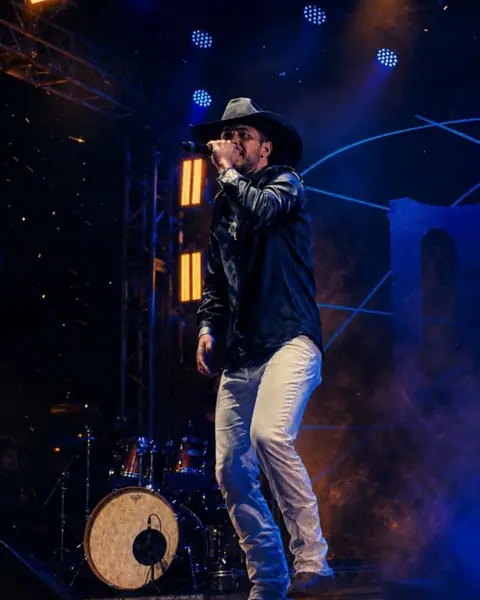 Cantor de chapéu no palco, com fumaça e luz