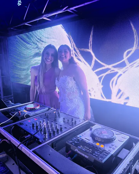 Duas mulheres atrás da mesa de DJ, com painel de LED ao fundo