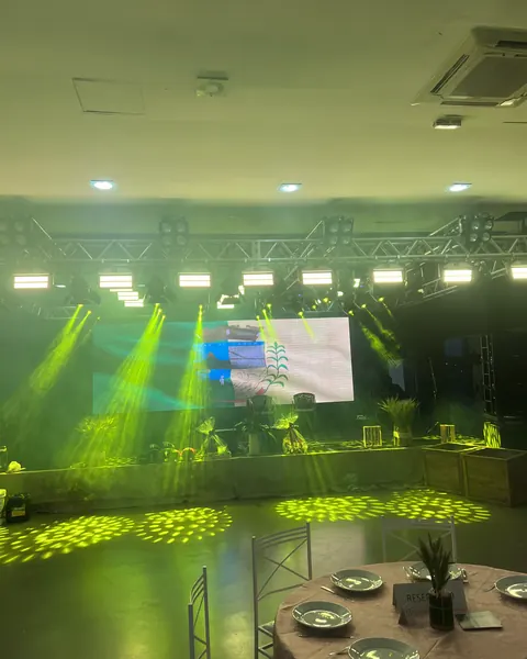 Salão de evento com painel de LED, iluminação em feixes e mesas postas