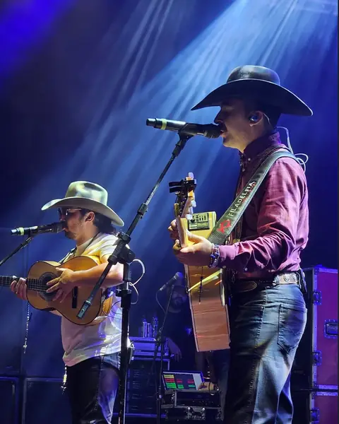 Dupla de chapéu cantando com violão no palco, com luz azul