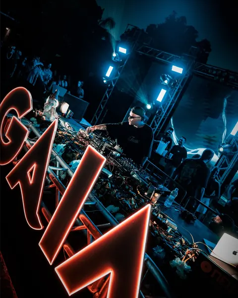 Letreiro GAIA em neon na frente da mesa de DJ, com luzes azuis e painel ao fundo