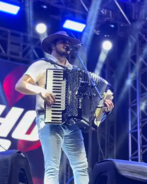 Cantor de chapéu tocando acordeão no palco, com treliça de luz e painel de LED