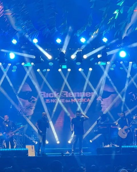 Dupla e banda no palco com painel de LED ao fundo e feixes de luz azul cruzados